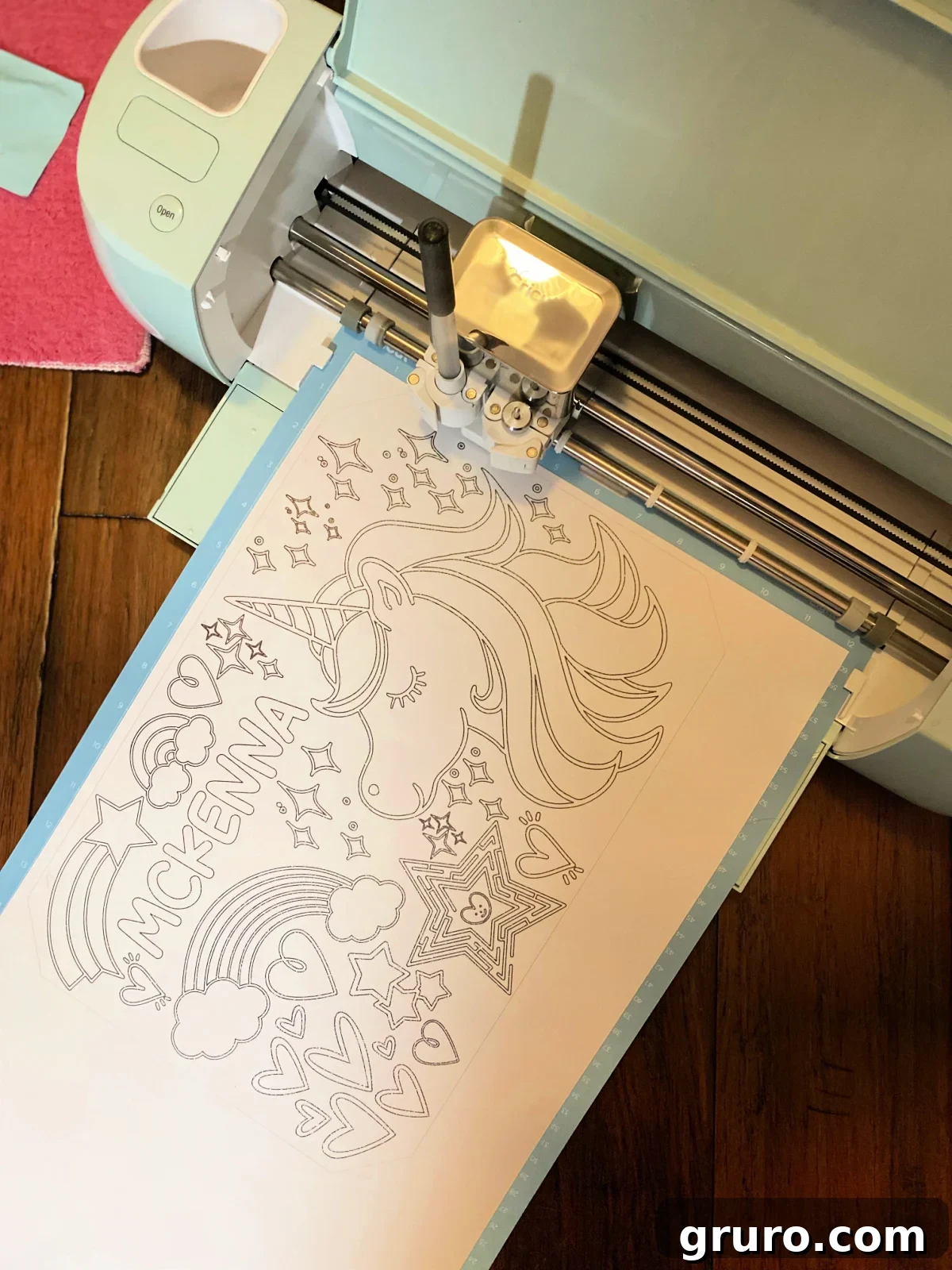 Green Cricut Explore Air writing with a black pen on a white paper.