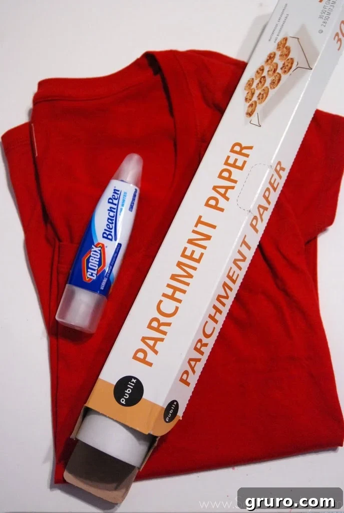Flat lay of essential supplies for a bleach pen t-shirt craft: a bleach pen for fabric design, a roll of parchment paper, and a plain dark t-shirt, neatly arranged on a light surface.