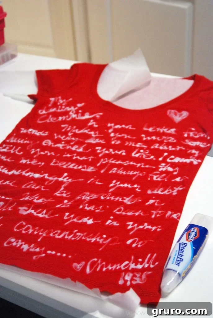 A dark t-shirt with partially bleached text visible after initial bleach pen application, showing the chemical reaction on the fabric and the custom design starting to emerge clearly.