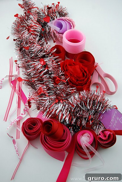 Craft supplies neatly arranged on a table, featuring a plain Valentine's garland, assorted red, pink, and purple ribbon scraps, and a pair of scissors.