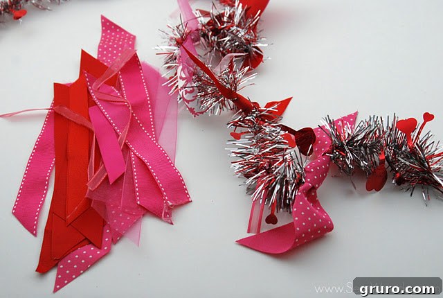 A plain tinsel garland laid out with various cut pink and red ribbon scraps, ready to be tied.