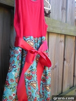 A child's dress in progress, showcasing the tank top bodice attached to the gathered paisley skirt with a decorative satin ribbon accent.