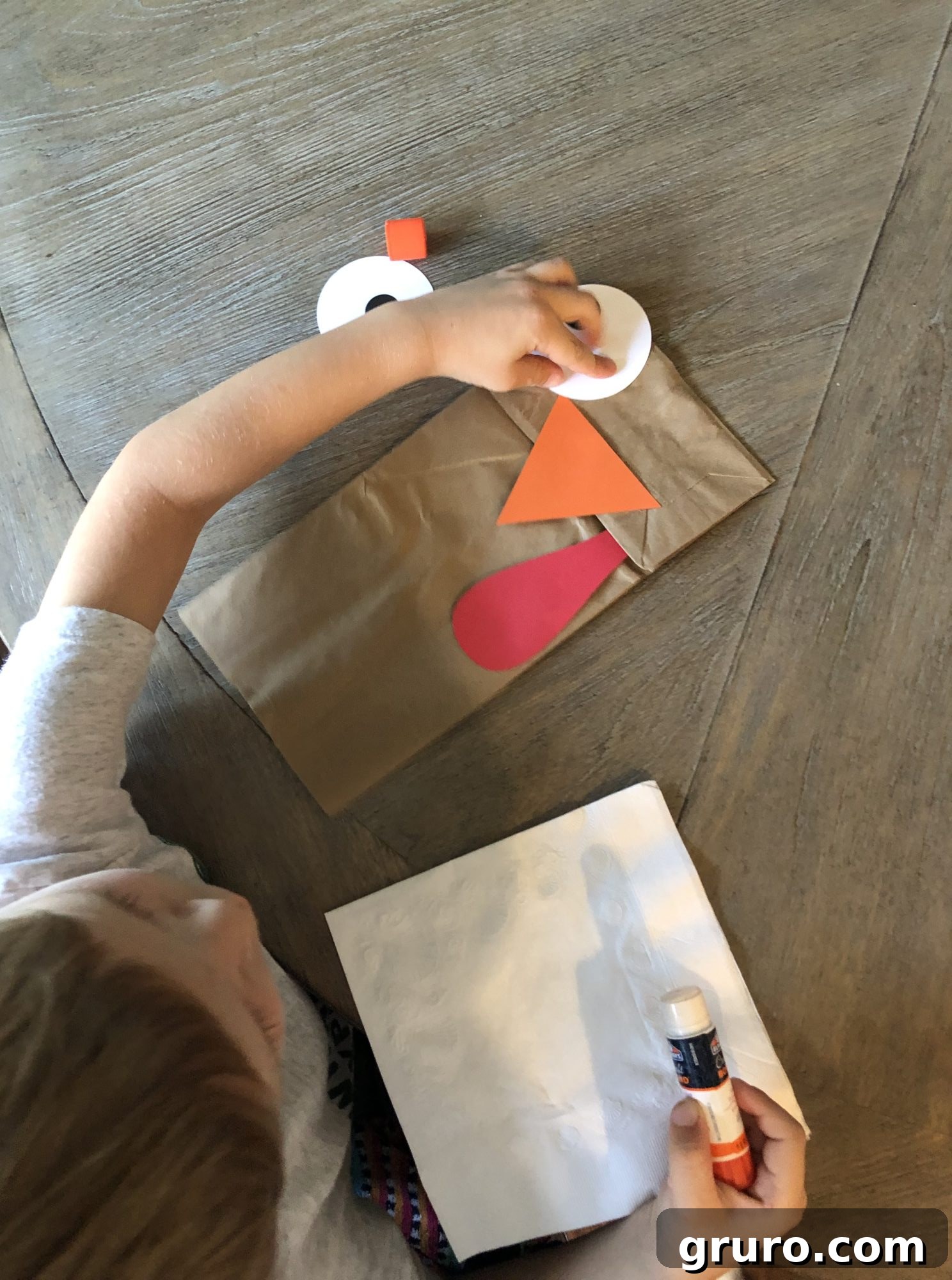 Exploring Turkey: Kids' Craft Adventures 3 Close-up of a child's hands gluing felt onto a paper bag for a turkey puppet craft, emphasizing hands-on activity