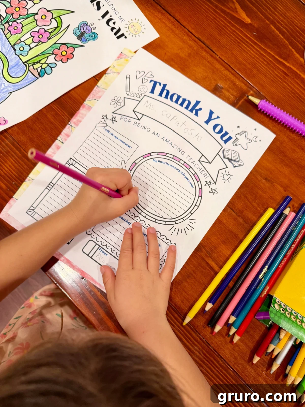 Printable Teacher Gratitude Gifts 3 Little girl filling out a thank you teacher printable using a colored pencil on a wooden table.