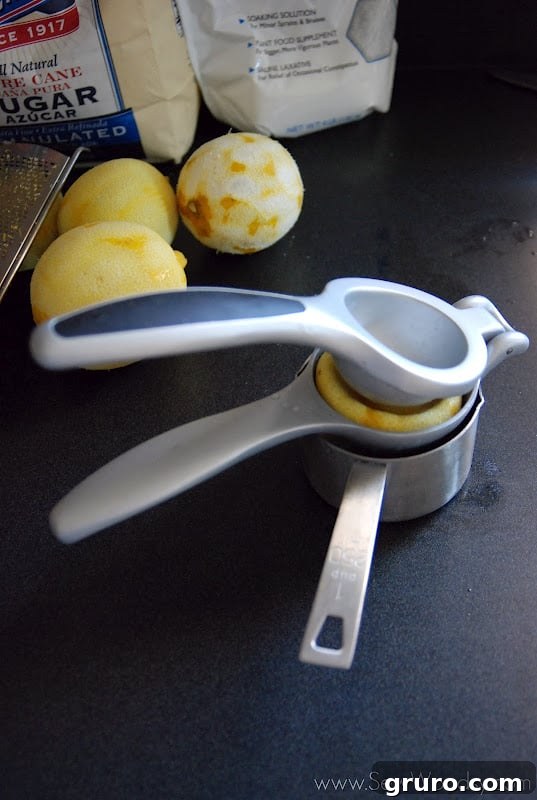A hand holding a juicer, extracting juice from half a lemon into the scrub mixture.