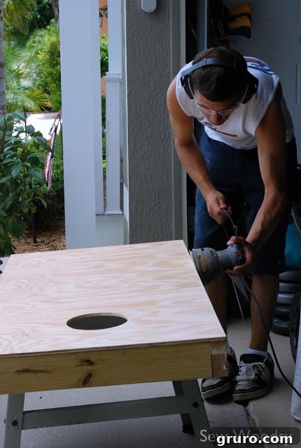Another view of a person diligently attaching the legs to a cornhole board