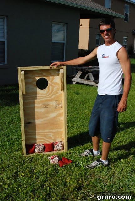 A person proudly demonstrating the foldable legs of his newly built cornhole board