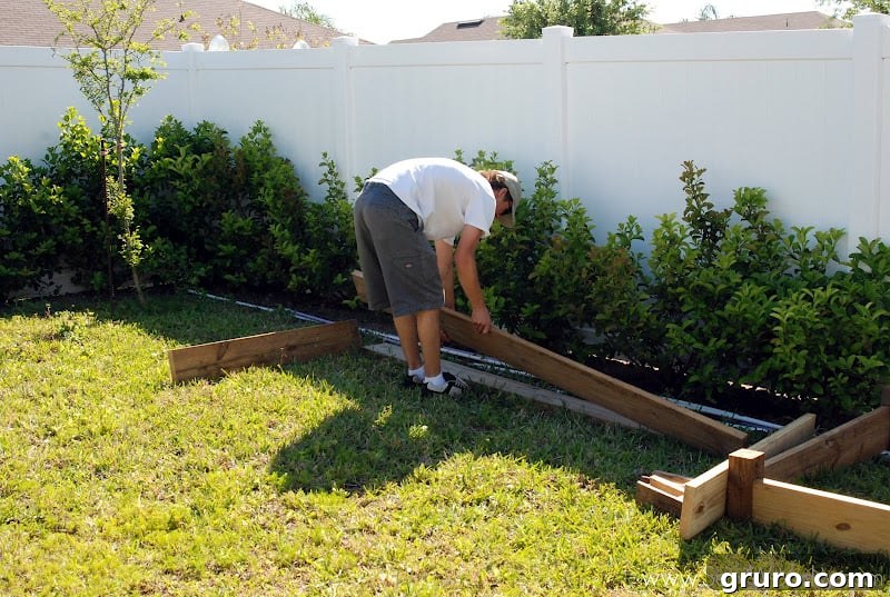 Mr. Woodsy arranging the wooden frames of the raised garden beds in the yard, carefully planning their placement.
