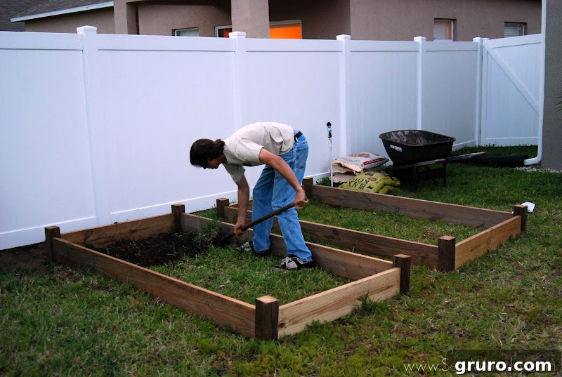 A section of yard with grass removed, exposing the soil and indicating preparation for a raised garden bed installation.