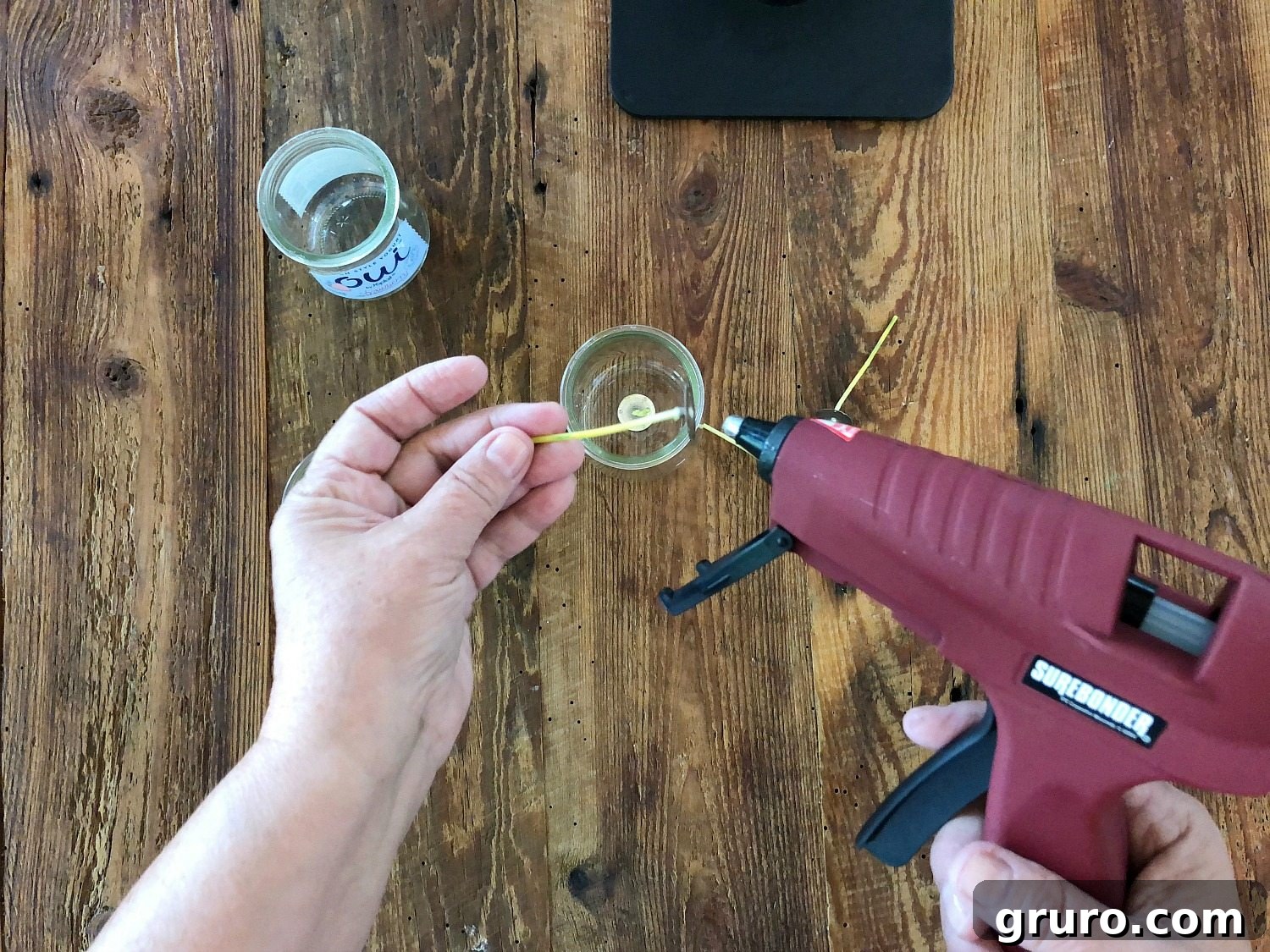Applying hot glue to the bottom of an Oui jar to secure the candle wick