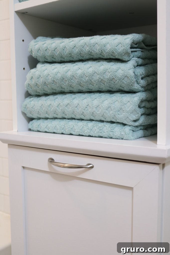 Bathroom storage with an integrated hamper and large aqua teal towels, enhancing decor on a budget.