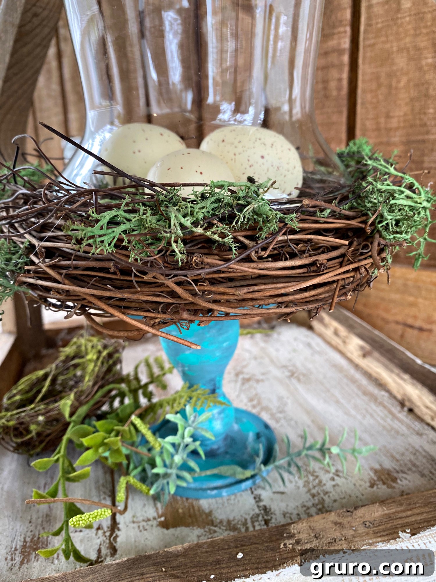 A bird nest with faux eggs and moss secured on a painted candlestick
