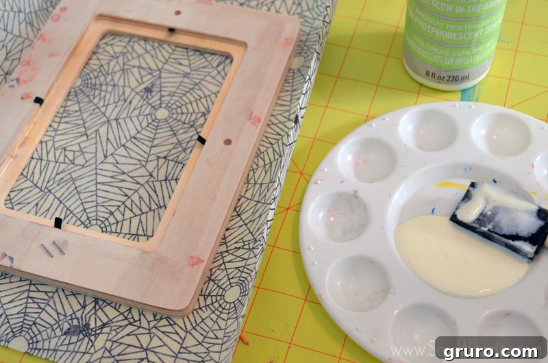 Measuring and cutting spider decoupage paper to fit a wood frame, leaving extra margin for wrapping, for a DIY Halloween project.