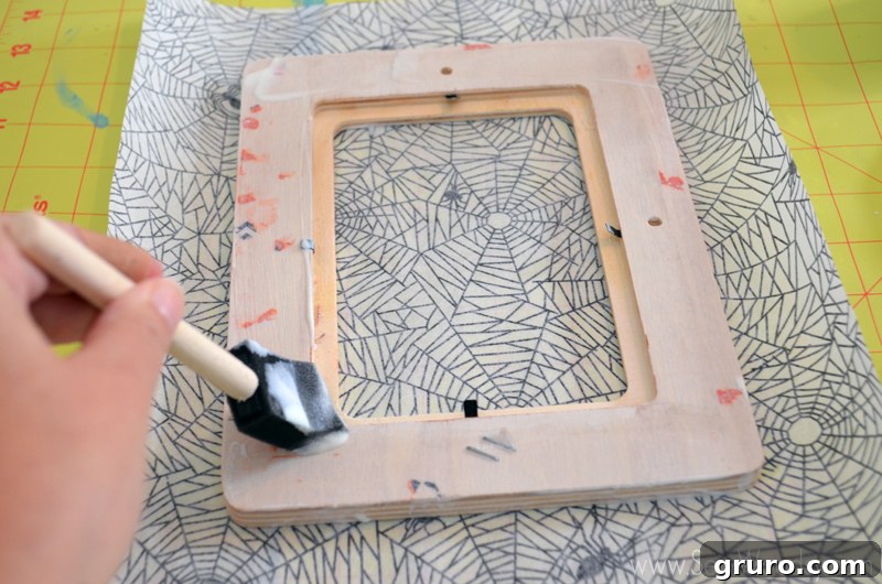 Placing the wood picture frame face down onto the cut spider decoupage paper, ensuring proper alignment for the Halloween craft.
