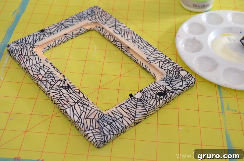 Folding the edges of the spider decoupage paper like a package onto the back of the frame and securing with decoupage glue.