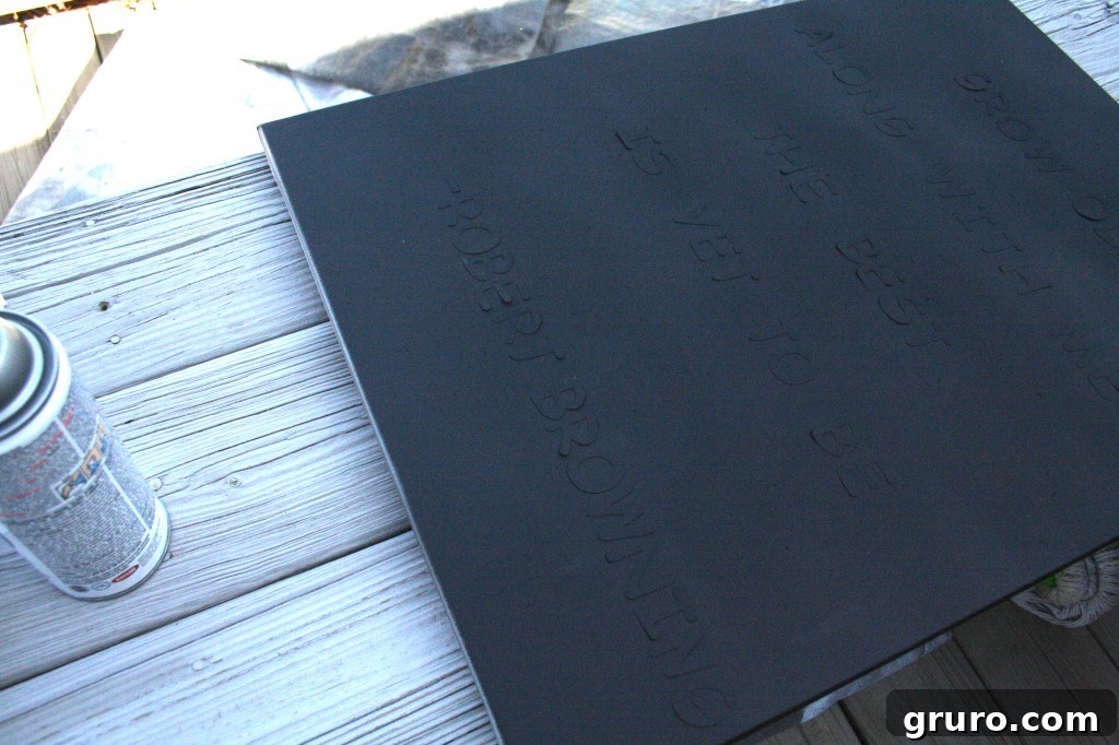 Close-up of a canvas being spray painted black over letter stickers, showcasing the DIY art process.