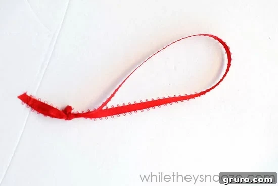 Tying a knot on the string inside the wooden box to secure the ornament hanger.