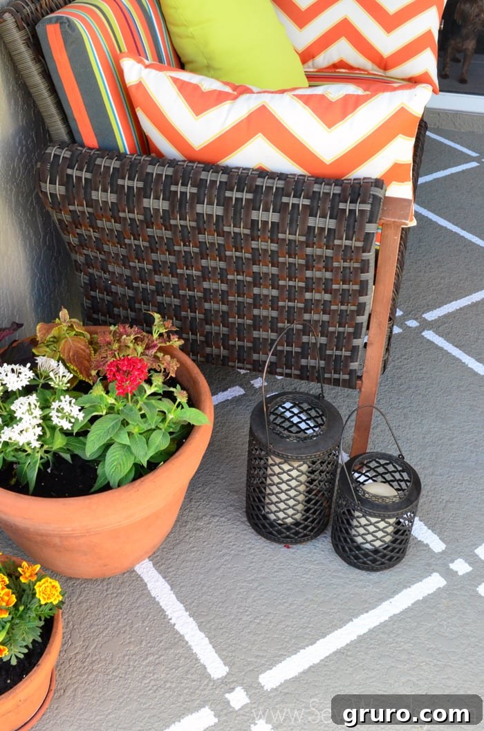 An outdoor couch with bright orange cushions, surrounded by lush plants in planters, decorative lanterns, and a striking painted pattern on the concrete floor.