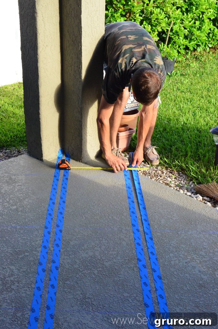 A person precisely applying blue painter's tape along a measuring tape and chalk lines on a patio floor.