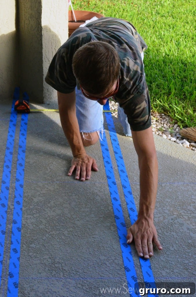 A person smoothing down blue painter's tape on a textured concrete patio surface with their hand, ensuring a tight seal.