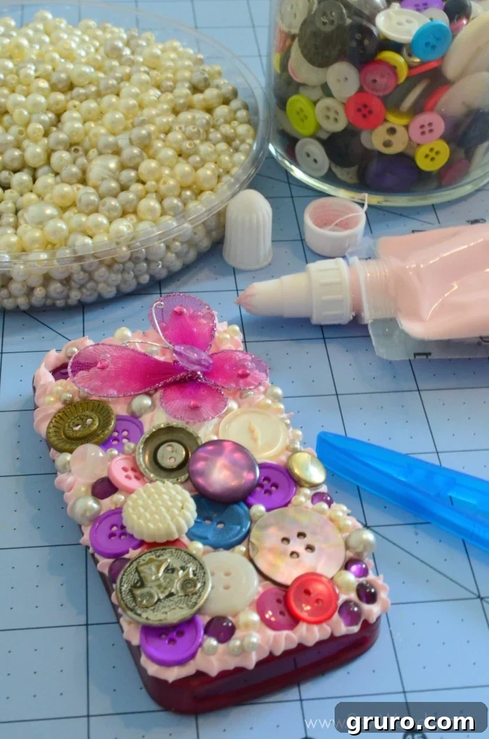 A fully embellished Decoden phone case, featuring a vibrant array of buttons, pearls, and purple gems, with a delicate 3D butterfly charm prominently placed as the central focal point. The photo captures the intricate details and rich textures of the design, completed before the application of any drizzle paint.