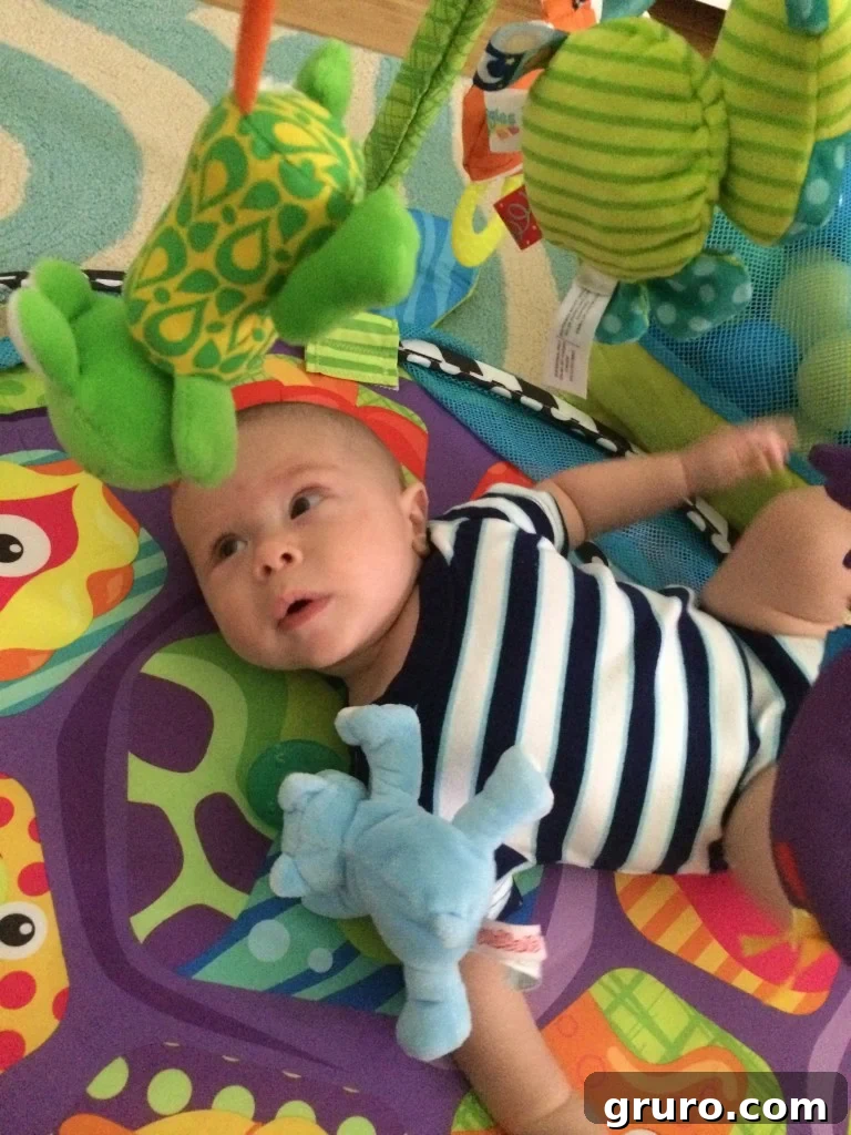 Baby Ryder happily playing on his activity mat while mom works on her computer nearby
