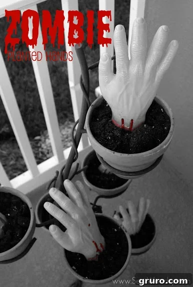 Two zombie hands reaching out of the ground in a garden bed, looking very realistic and creepy.