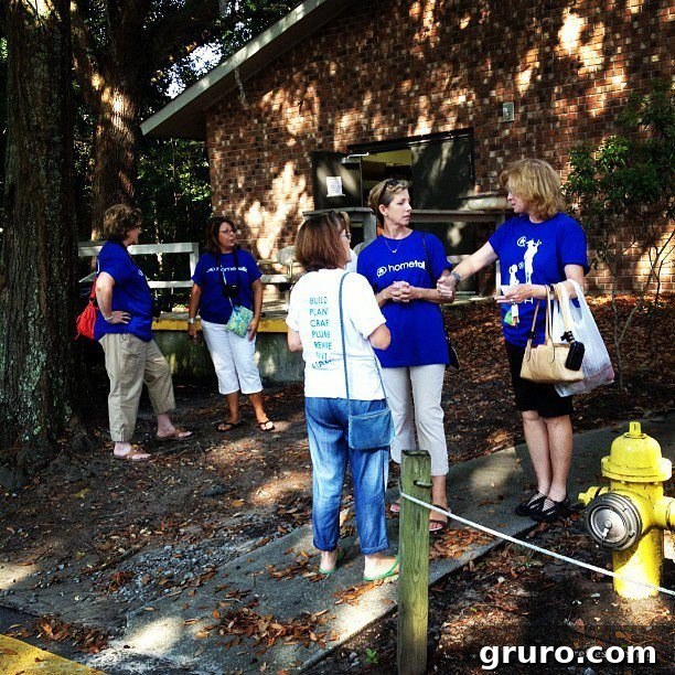 Women gathered outside a building, discussing items in bags and hands