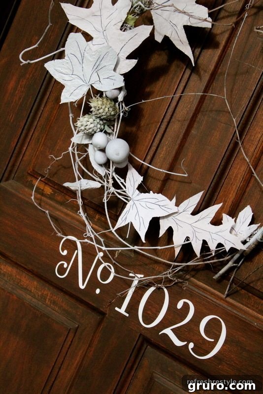 A completed white natural wreath, elegantly hanging by a ribbon on a dark door.