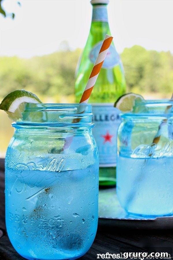 Refreshing drinks served in beautiful blue mason jars, garnished with lime slices and colorful straws, perfect for an outdoor gathering.