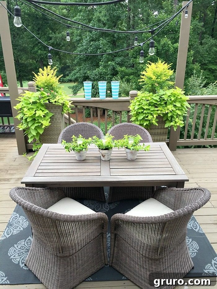 Perfect outdoor dining space illuminated with string lights, candles, and lush greenery. A beautiful centerpiece of candles nestled within garden pots enhances the ambiance.