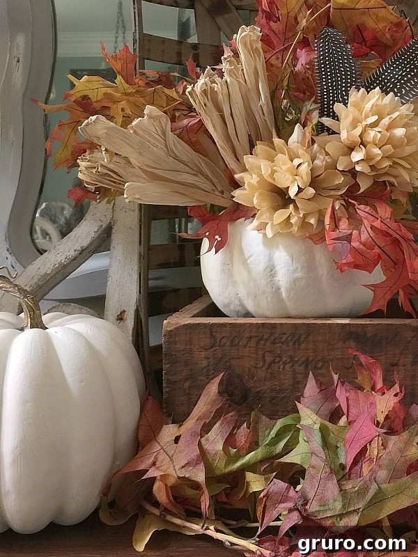 Detailed View of Feather and Floral Accents in Pumpkin Decor Close-up of decorative feathers, mums, and corn husks arranged beautifully in a painted white pumpkin