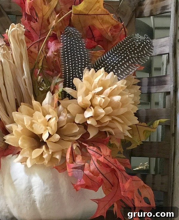 Fall Foliage in White Pumpkin: A Simple and Elegant Display Side view of a refurbished white pumpkin filled with rich fall leaves, colorful mums, and rustic feathers