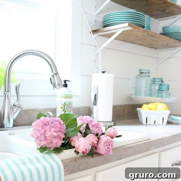 A beautifully decorated summer farmhouse kitchen with white shiplap walls and open shelving, featuring fresh flowers and turquoise accents.