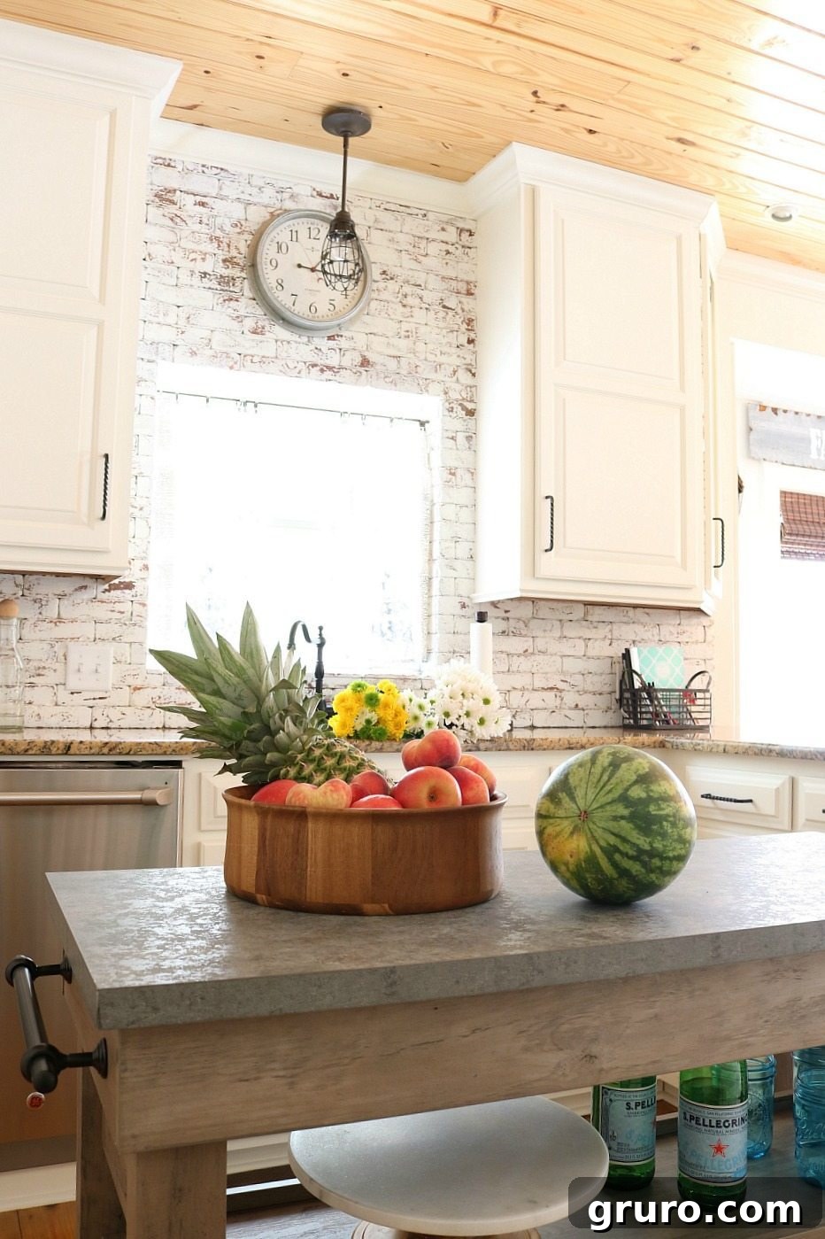 Painted brick backsplash, shiplap ceiling, and white cabinets define this farmhouse kitchen with a practical island