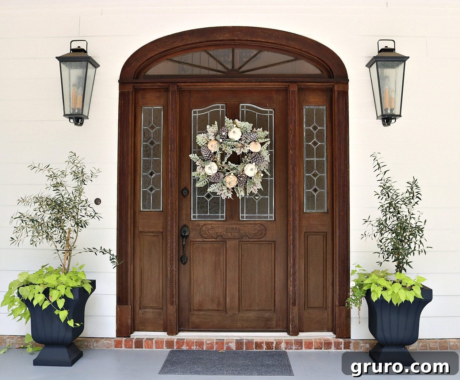 Olive trees flanking an entry with a pale fall wreath, creating a soft autumn welcome.