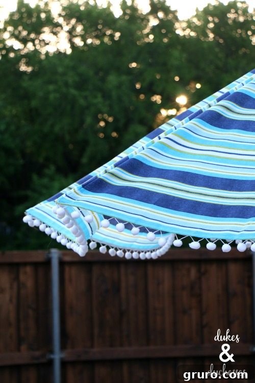 A vibrant DIY embellished umbrella with colorful pom pom trim, providing shade and style to an outdoor setting.