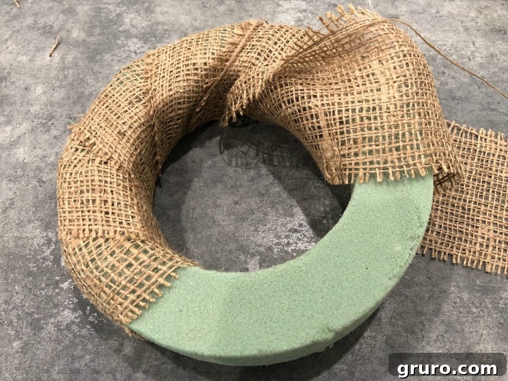 Wrapping a foam wreath form with natural burlap ribbon to create a rustic base for a DIY farmhouse candle ring, showcasing the first step of the crafting process