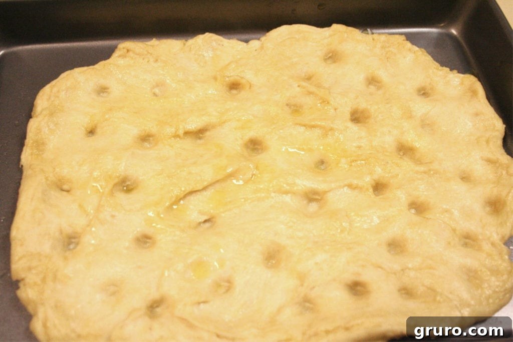 Hands pressing dimples into focaccia dough on a baking sheet
