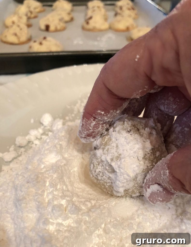 Rolling warm Pecan Snowball Cookies in powdered sugar